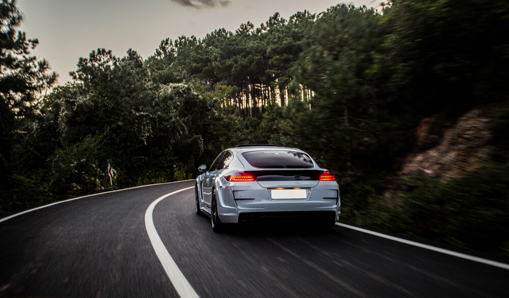 Silver sedan driving on a scenic forest road, representing a smooth car rental journey with GTG.